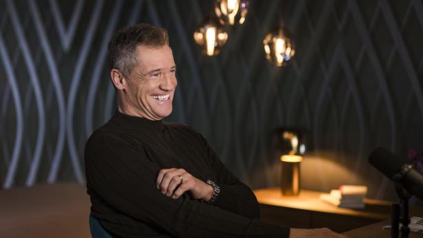 Armin Assinger in einem schwarzen Pullover, lachend