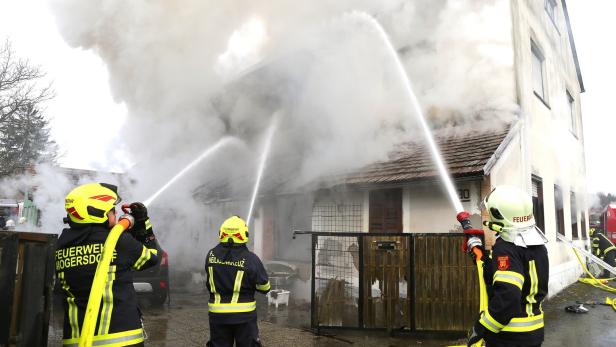 Drei Feuerwehrleute löschen mit Wasserschläuchen ein brennendes, stark verrauchtes Wohnhaus.