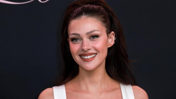 Nicola Peltz trägt ein trägerloses schwarzes Kleid und baumelnde Ohrringe.