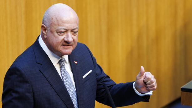 Ein Mann im Anzug mit Österreich-Anstecker gestikuliert vor einem Mikrofon mit erhobenem Daumen.