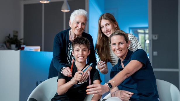 Vier Personen unterschiedlichen Alters halten gemeinsam Zahnbürsten und lächeln in die Kamera.