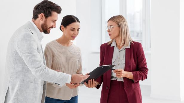 Drei Personen stehen zusammen und betrachten gemeinsam ein Klemmbrett in einem hellen Raum.