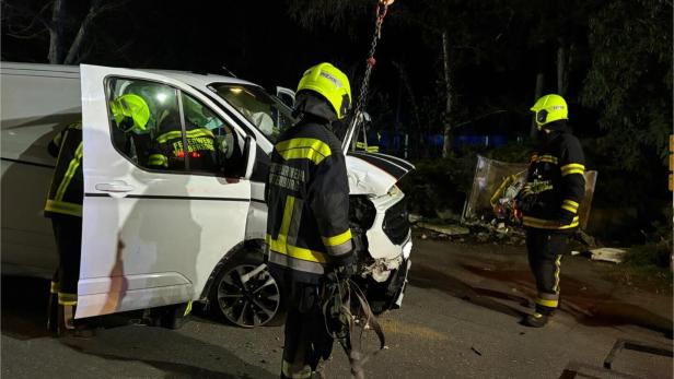 Drei Feuerwehrleute arbeiten nachts an einem stark beschädigten weißen Transporter nach einem Unfall.