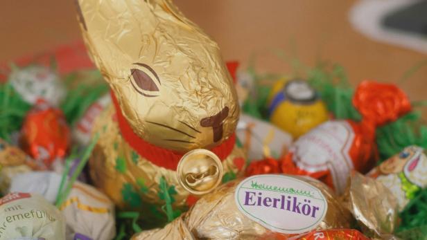 Ein goldener Lindt-Osterhase steht zwischen verschiedenen bunten Ostersüßigkeiten in einem Nest aus grünem Kunstgras.