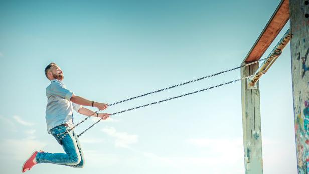 Ein Mann schaukelt an einer hohen Schaukel in der Luft vor blauem Himmel.