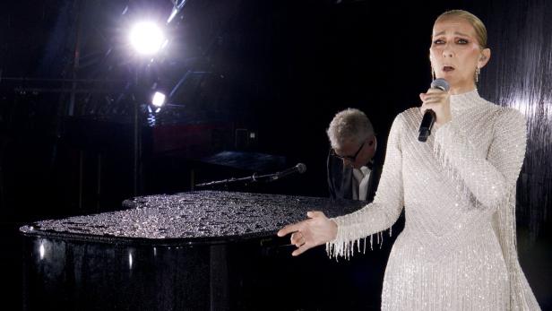 Céline Dion singt in einem glitzernden Kleid neben einem Pianisten vor einem Klavier.