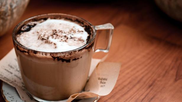 Eine Tasse heiße Schokolade mit Schaum und Schokoladenpulver auf einem Holztisch.