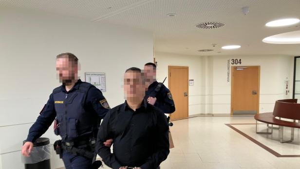 Ein Mann in Handschellen wird von zwei Polizisten durch einen Gerichtsflur geführt.