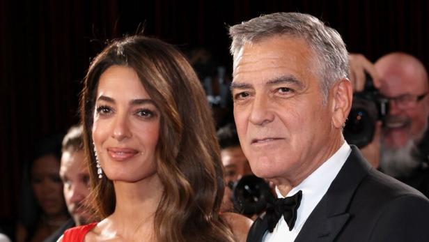 Amal Clooney und George Clooney posieren auf einem roten Teppich.