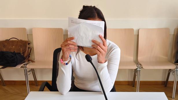 Junge Frau mit Papier vor dem Gesicht im Gerichtssaal.