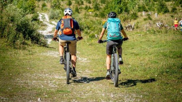 Zwei Radfahrer fahren auf einem Weg vor einer Bergkulisse.