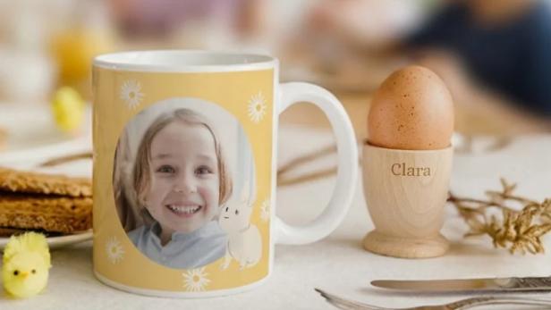 Personalisierte Tasse mit Kinderfoto und Eierbecher mit dem Namen Clara auf einem Frühstückstisch.