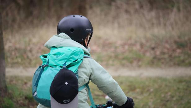 Ein Kind mit Helm und Rucksack fährt mit dem Fahrrad auf einem Weg durch die Natur.