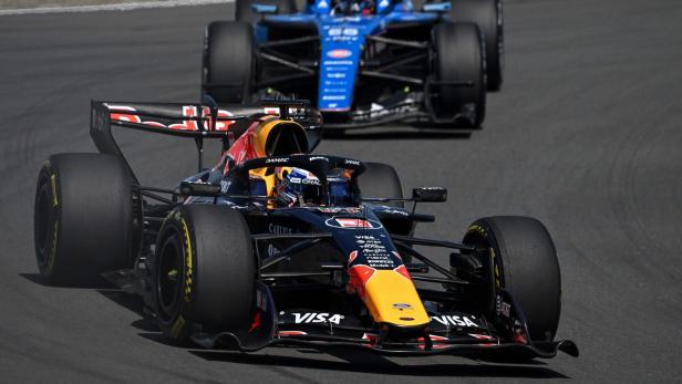 Zwei Formel-1-Autos fahren dicht hintereinander auf einer Rennstrecke, eines schwarz-rot, das andere blau.