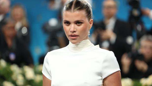 Sofia Richie mit zurückgekämmten Haaren trägt ein weißes Kleid und Ohrringe.