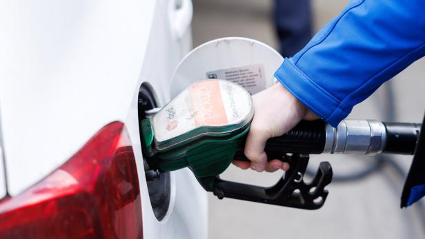 Eine Person tankt ein weißes Auto mit einer grünen Zapfpistole an einer Tankstelle.