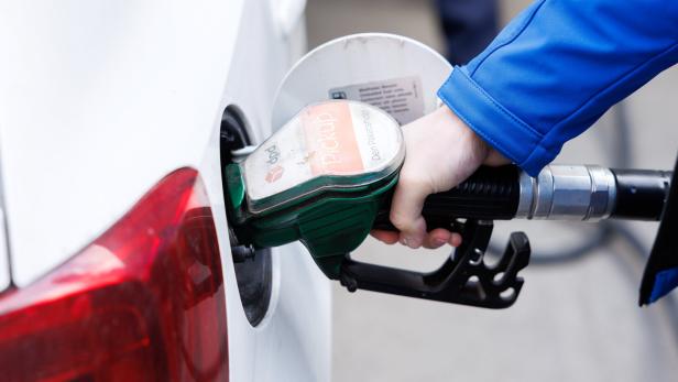 Eine Person tankt ein weißes Auto mit einer grünen Zapfpistole an einer Tankstelle.