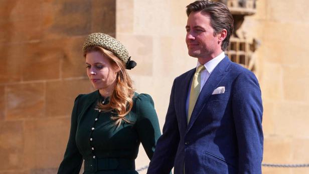 Prinzessin Beatrice im grünen Kleid mit Hut und Handtasche geht Hand in Hand mit einem Mann im blauen Anzug auf einem Gehweg.