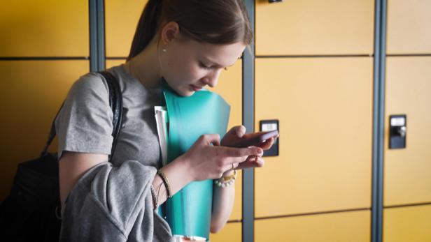 Schülerin schaut auf ihr Smartphone vor gelben Spints