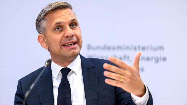 Ein Mann im Anzug spricht gestikulierend vor einem Mikrofon, im Hintergrund unscharfer Schriftzug.