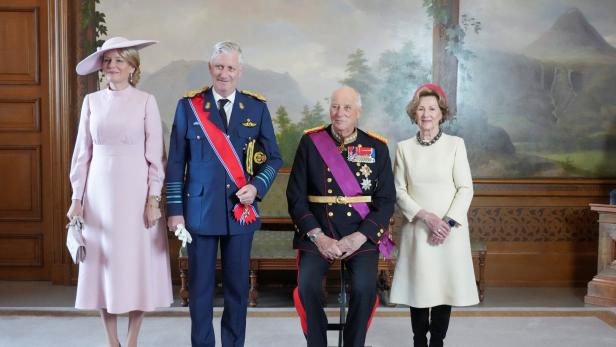 Königin Sonja und König Harald V. mit König Philippe und Königin Mathilde. Alle sind elegant gekleidet. Harald sitzt, die anderen Personen stehen.