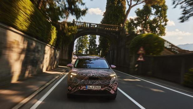 Getarnter Skoda Peaq fährt auf einer sonnigen Straße am Comer See unter einer Steinbrücke.