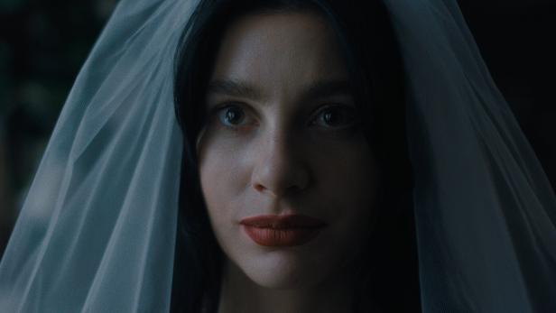 Rachel mit dunklen Haaren und rotem Lippenstift trägt einen Schleier.