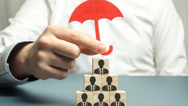 Boss holding a red umbrella and defending his team with a gesture of protection. Security and safety in a business team. Life insurance. Customer care, care for employees. Wooden blocks