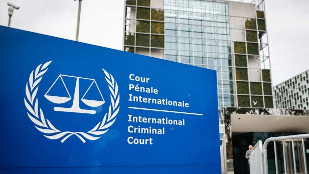 Blaues Schild mit dem Logo des Internationalen Strafgerichtshofs vor einem modernen Bürogebäude mit Glasfassade.