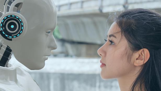 Eine Frau und ein humanoider Roboter stehen sich gegenüber und schauen sich intensiv in die Augen.