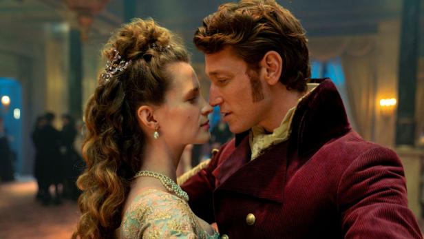 Ein elegant gekleidetes Paar tanzt eng umschlungen und blickt sich verliebt in die Augen.