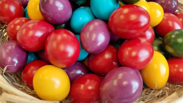 Ein Korb ist gefüllt mit bunten Ostereiern in Rot, Gelb, Lila, Grün und Türkis.