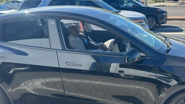 Eine Person schläft am Steuer eines schwarzen Tesla an einer belebten Straßenkreuzung.