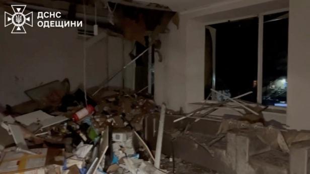 Ein zerstörtes Zimmer mit Trümmern, herabgestürzter Decke und zerbrochenem Fenster in der Nacht.