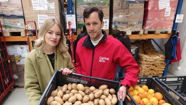 Zwei Personen halten eine Kiste mit Kartoffeln in einem Lagerraum mit Lebensmitteln.