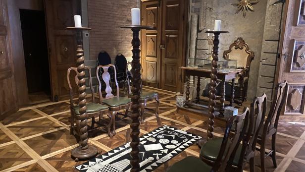 Ein Raum mit Stühlen im Kreis um einen Teppich, flankiert von Kerzenständern.