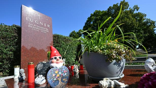 Auf dem Grabstein von Richard Lugner stehen Grablichter, ein Gartenzwerg und ein Topf mit Pflanzen.
