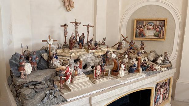 Mehrere Figuren stellen die Kreuzigung Jesu und Szenen seines Leidenswegs auf einem steinernen Podest mit Kreuzen und römischen Soldaten dar.