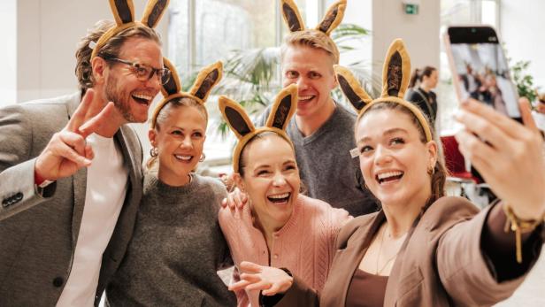 Fünf lachende Erwachsene mit Hasenohren-Stirnbändern machen gemeinsam ein Selfie.