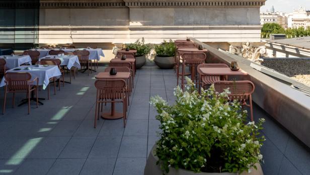 Ein Dachterrassen-Restaurant mit Tischen und Stühlen befindet sich unterhalb eines Gebäudes mit Skulpturen.