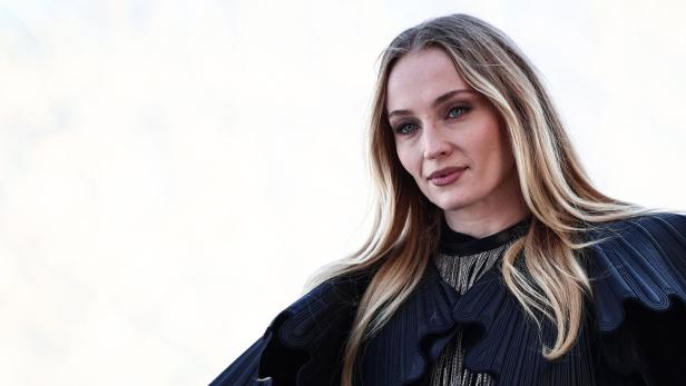 Sophie Turner mit blondem Haar und einem schwarzen Oberteil blickt zur Seite.