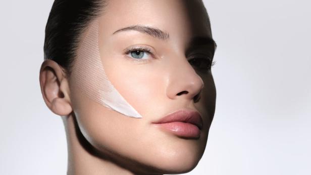 Frau mit glatter Haut und Creme auf der Wange, teilweise im Schatten.