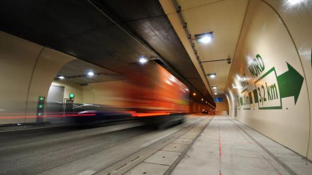Ein Lastwagen fährt schnell durch einen beleuchteten Straßentunnel mit grünen Richtungsschildern an der Wand.