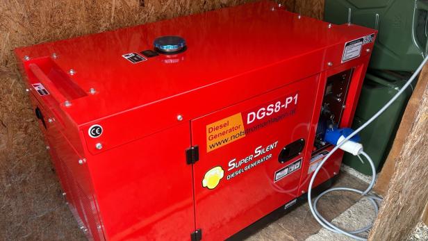 Roter Dieselgenerator mit der Aufschrift „Super Silent“ steht in einer Holzhütte und ist mit einem Stromkabel verbunden.