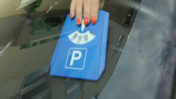 Eine Hand mit rotem Nagellack legt eine blaue Parkscheibe ins Auto.