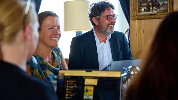 Mehrere Personen sitzen lachend an einem Tisch mit Laptops in einem hellen Raum.