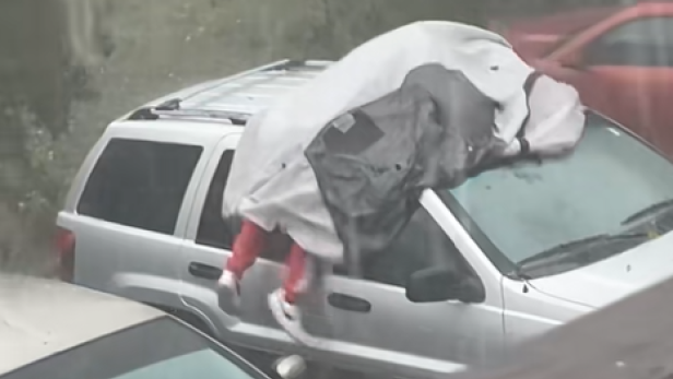 Person liegt mit Plane auf Autodach während starkem Hagel.