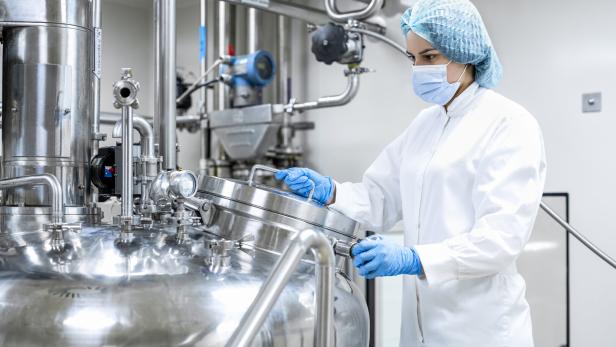 Eine Person in Schutzkleidung arbeitet an einem großen Edelstahltank in einer sterilen Produktionsumgebung.