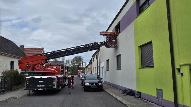 Ein Feuerwehrfahrzeug mit ausgefahrener Drehleiter steht vor einem Wohnhaus, die Leiter reicht zu einem Fenster im ersten Stock.