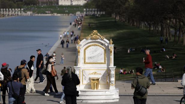 Eine prunkvolle Toilette mit goldenen Verzierungen steht im Freien, umgeben von vielen Menschen und Grünflächen.